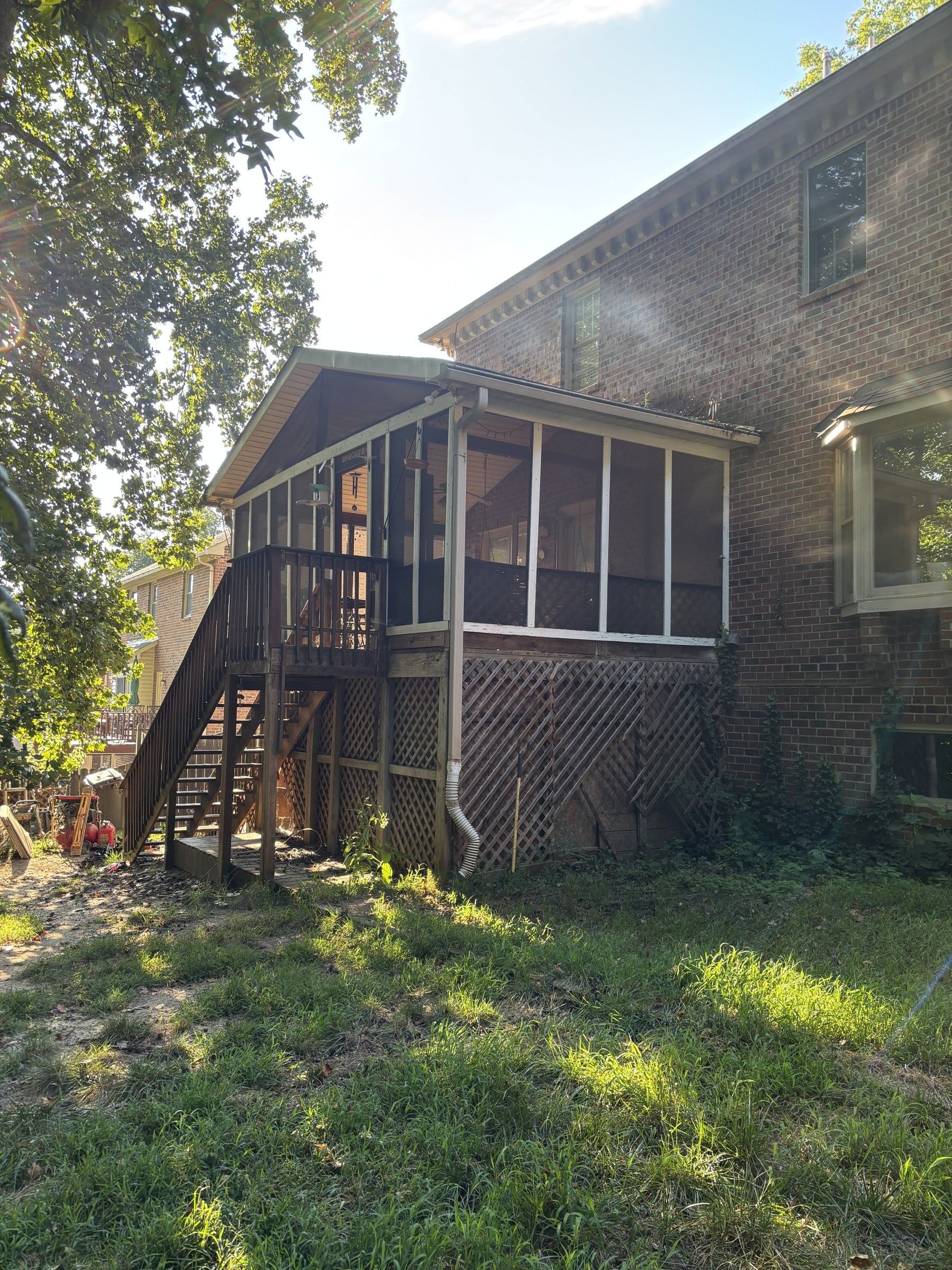 The original screened porch before the rebuild, with weathered framing, lattice skirting and an overgrown yard