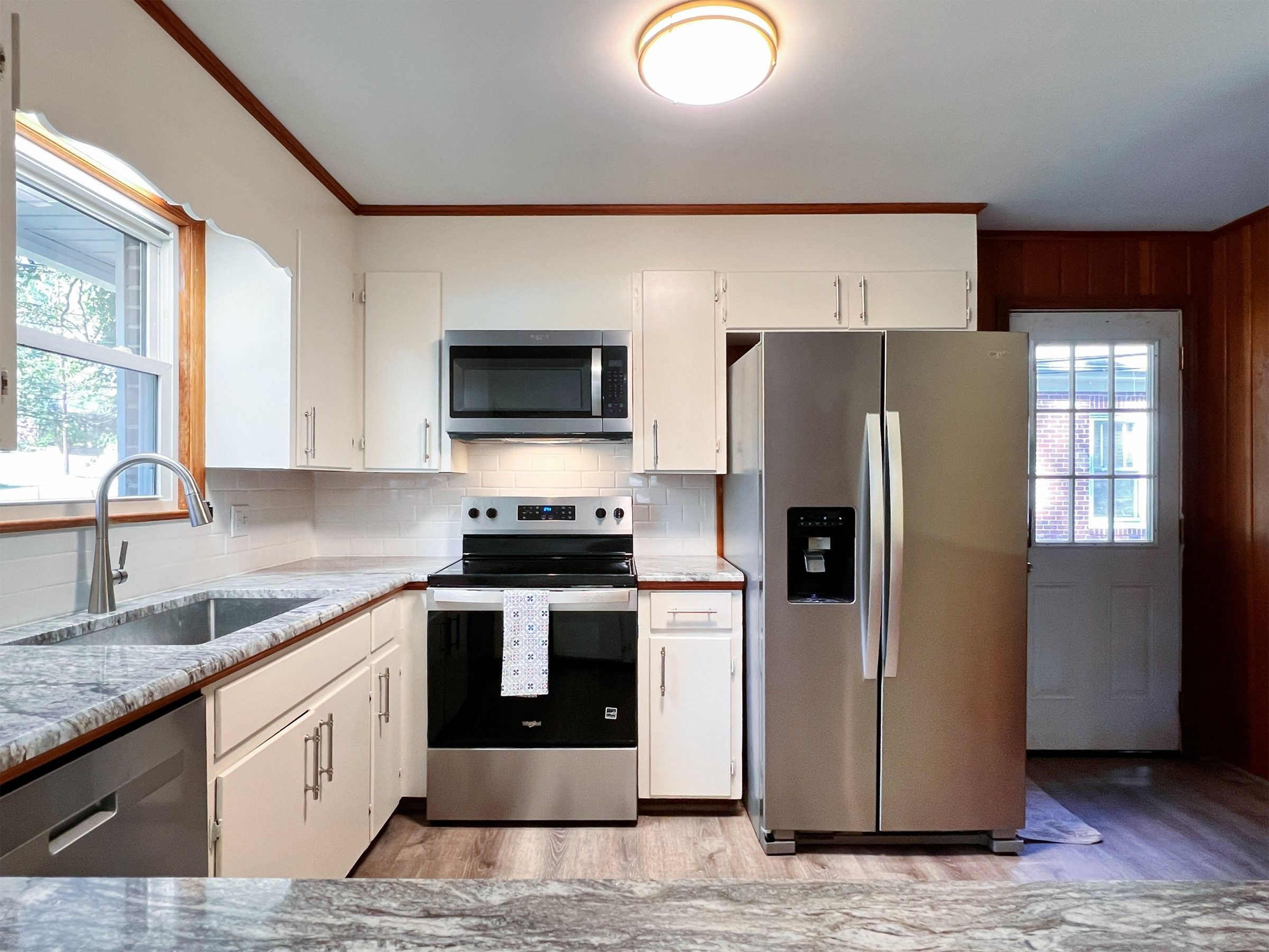 Range wall with a stainless microwave, range and refrigerator between white cabinets