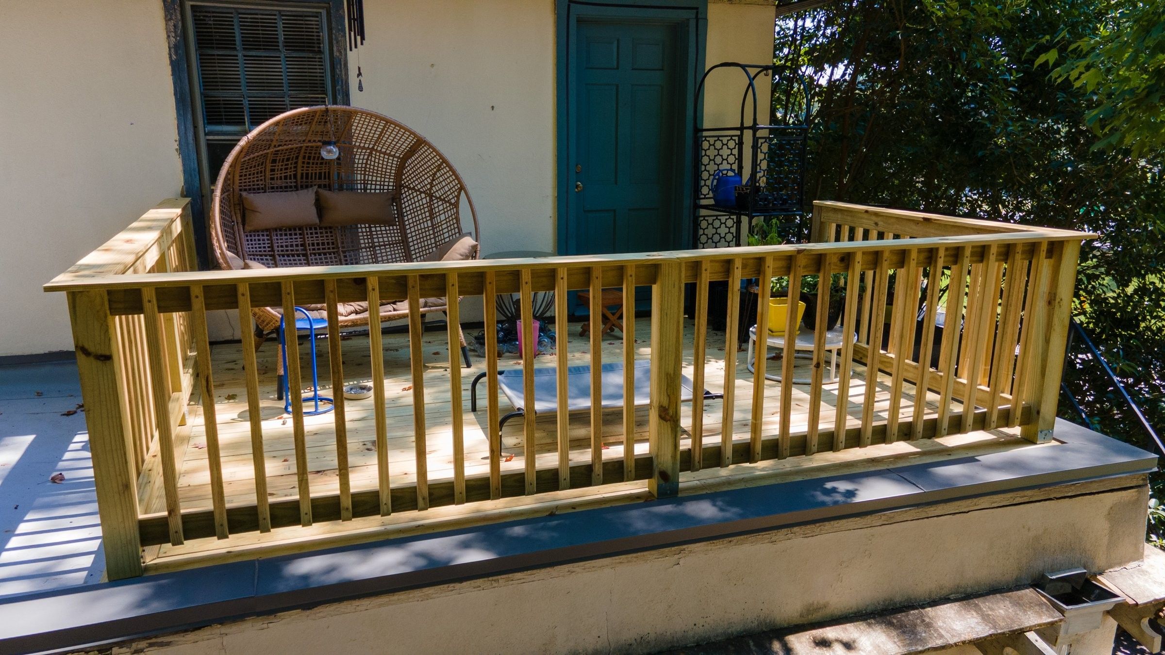 New wooden rooftop deck with a picket railing, a hanging egg chair and potted plants