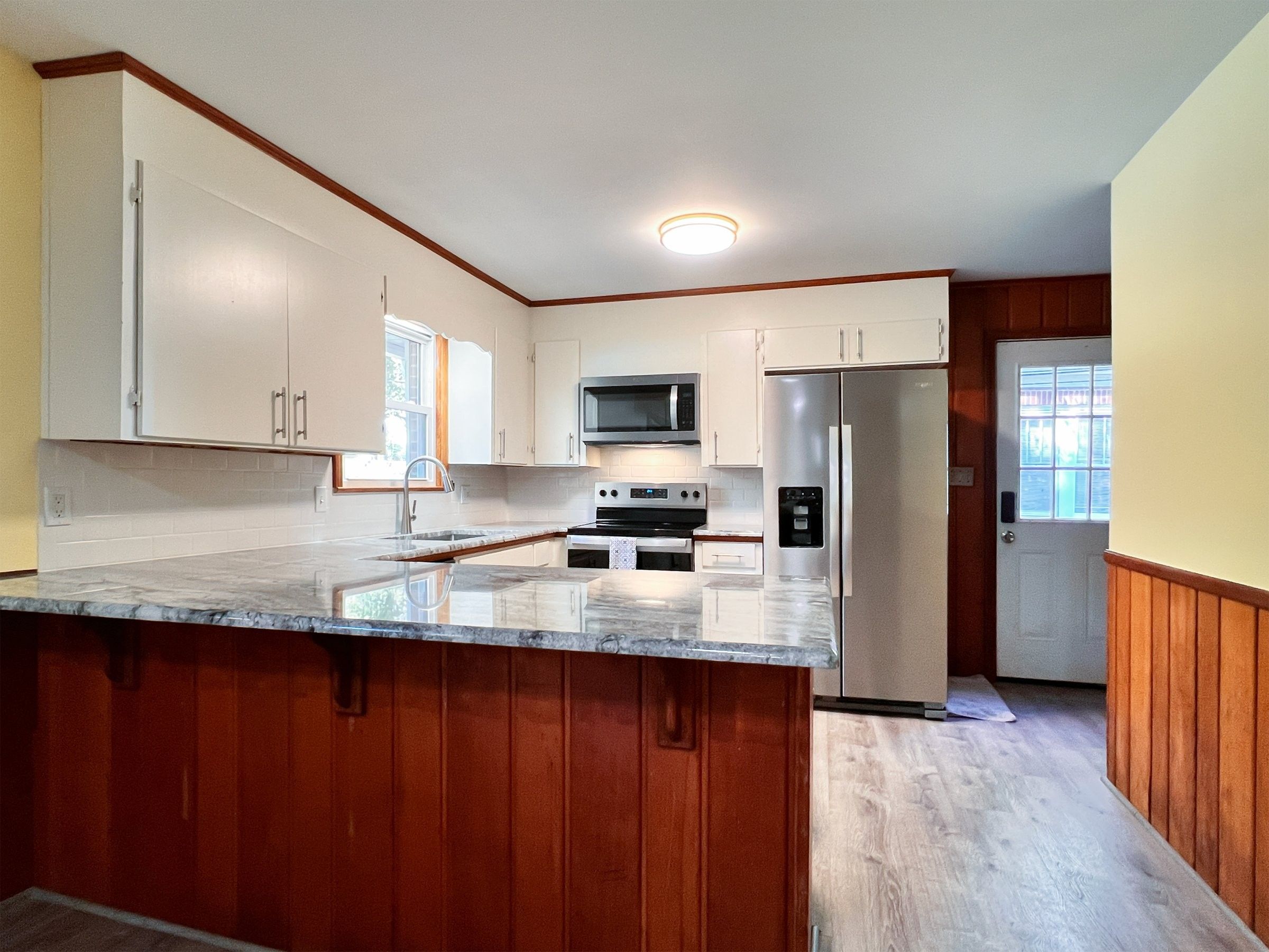 Kitchen with white cabinets, gray granite counters and a peninsula clad in warm wood paneling